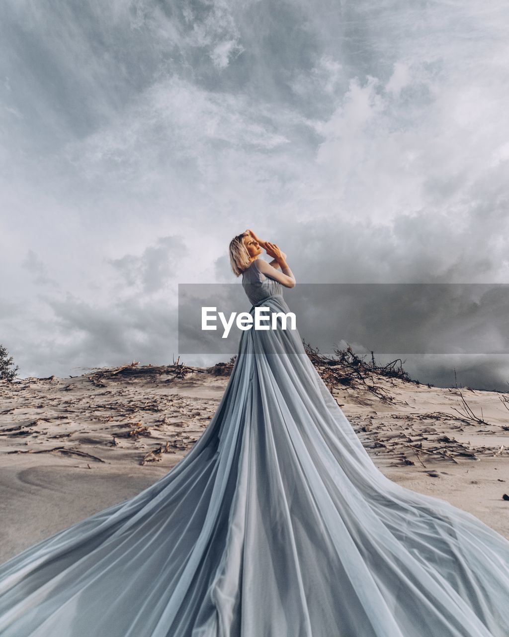 WOMAN STANDING ON SAND DUNES IN DESERT