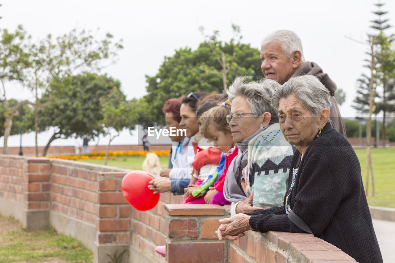 Friends looking away while standing by brick wall in park