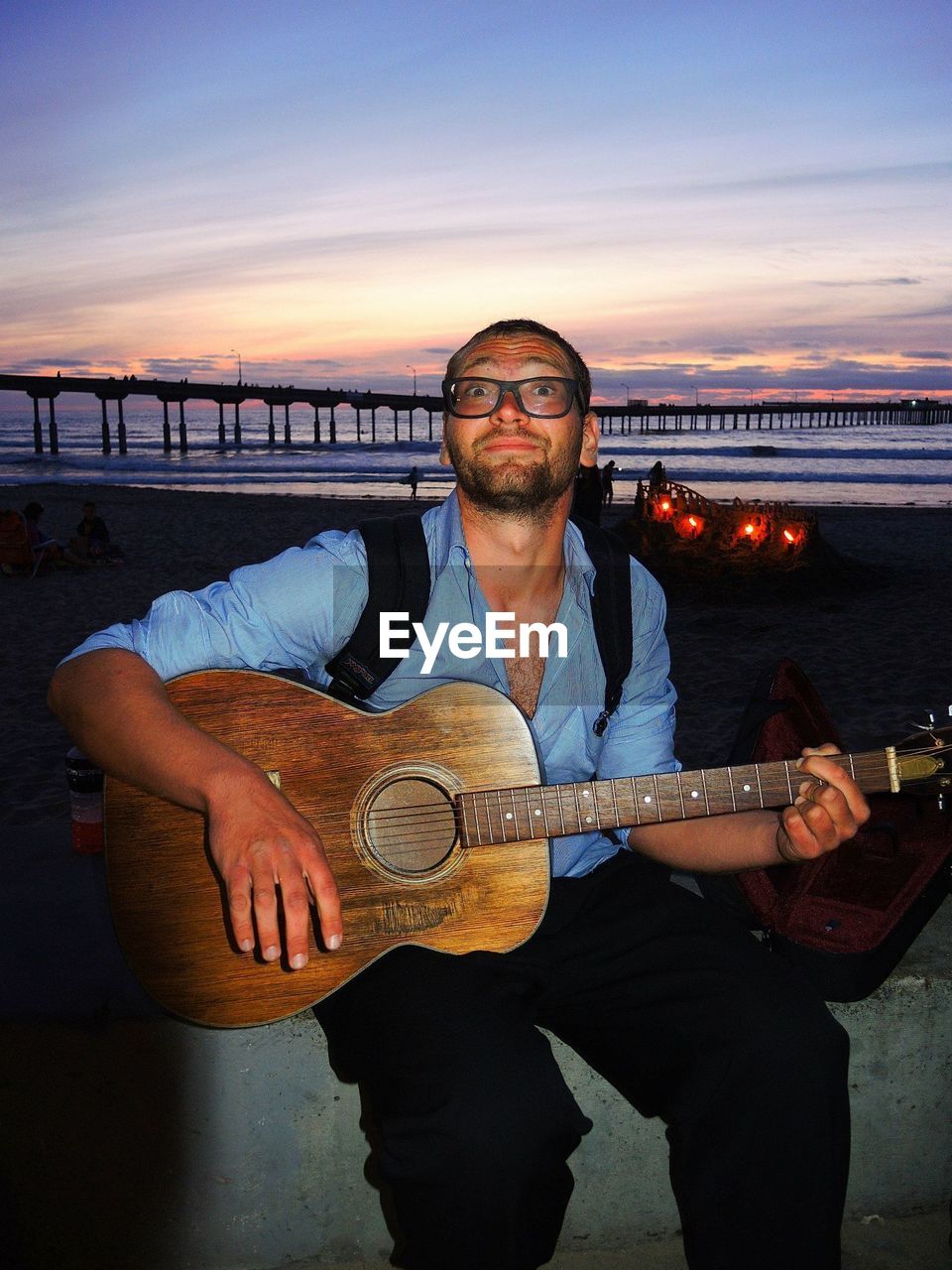 FULL LENGTH OF MAN SITTING ON GUITAR AGAINST SKY