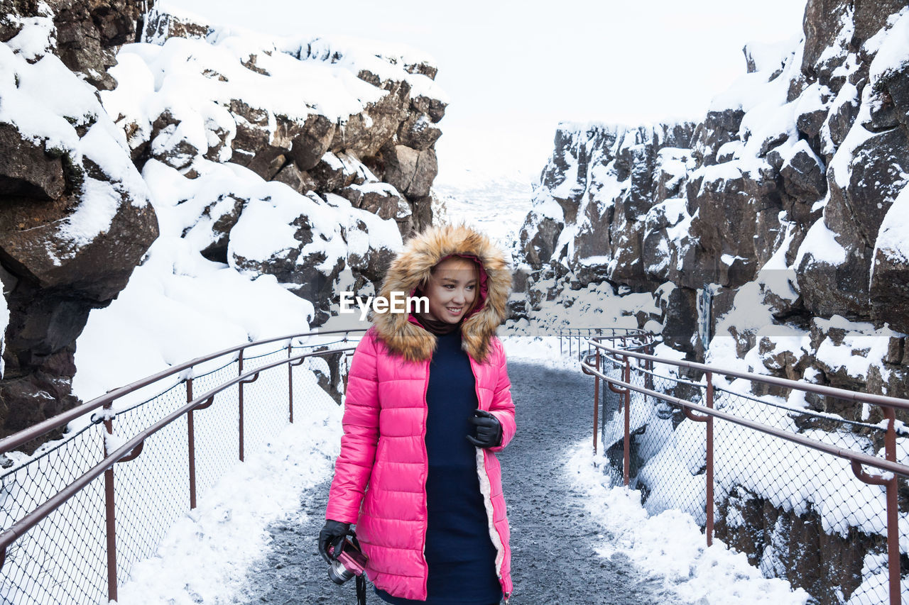 Smiling woman in warm clothes standing on snow covered bridge