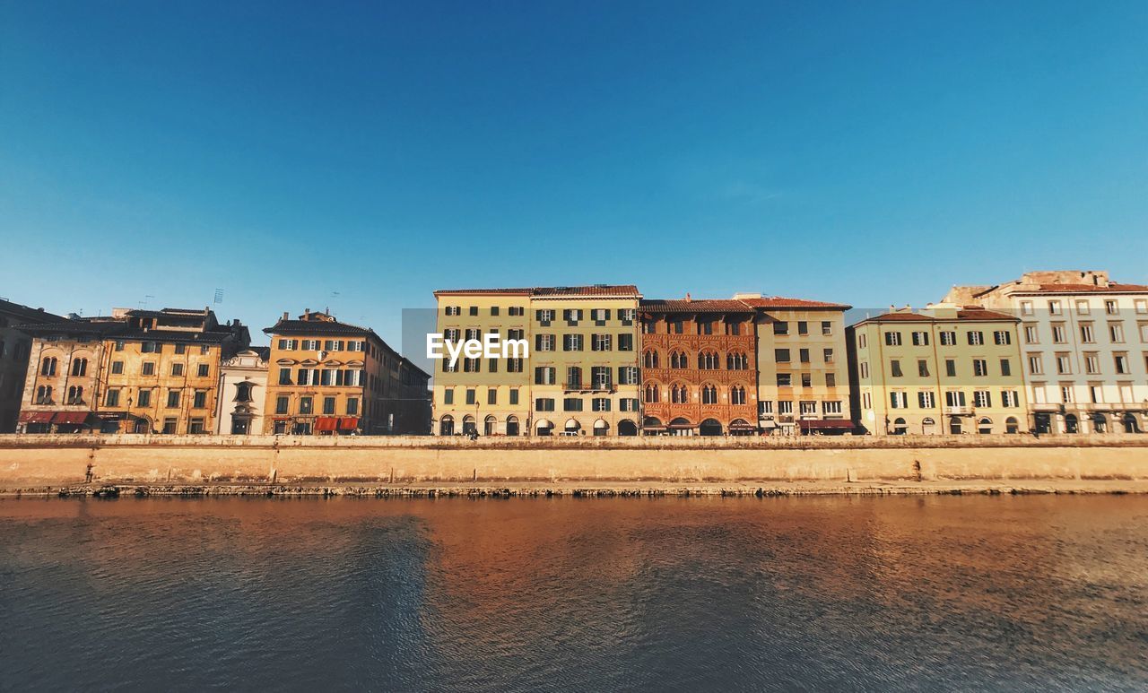 Buildings by river against clear blue sky