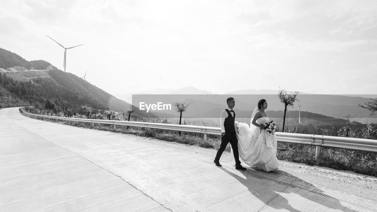 REAR VIEW OF COUPLE WALKING ON MOUNTAIN