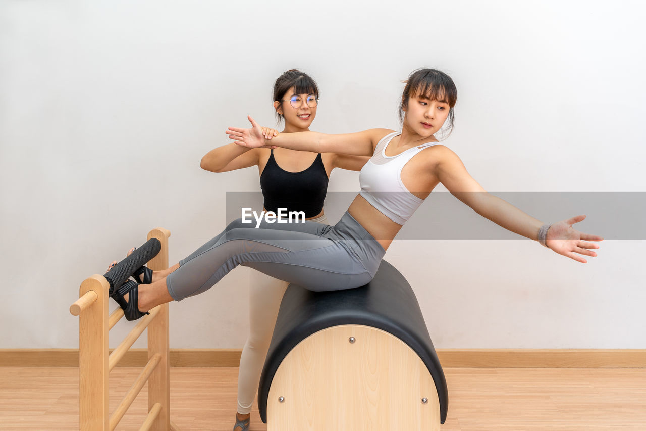 Young woman working on pilates ladder barrel machine with female trainer during health training
