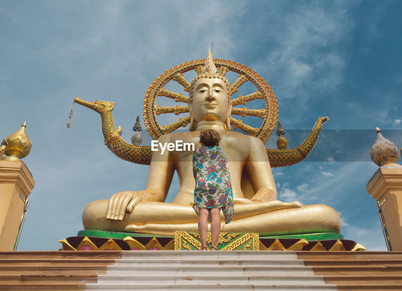 Low angle view of woman standing by buddha statue at temple against sky