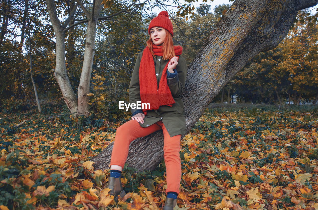 Autumn fashion portrait of stylish woman in bright orange knitted hat and scarf sitting 