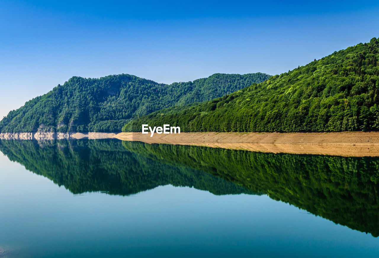 Scenic view of mountains reflecting in lake against clear sky