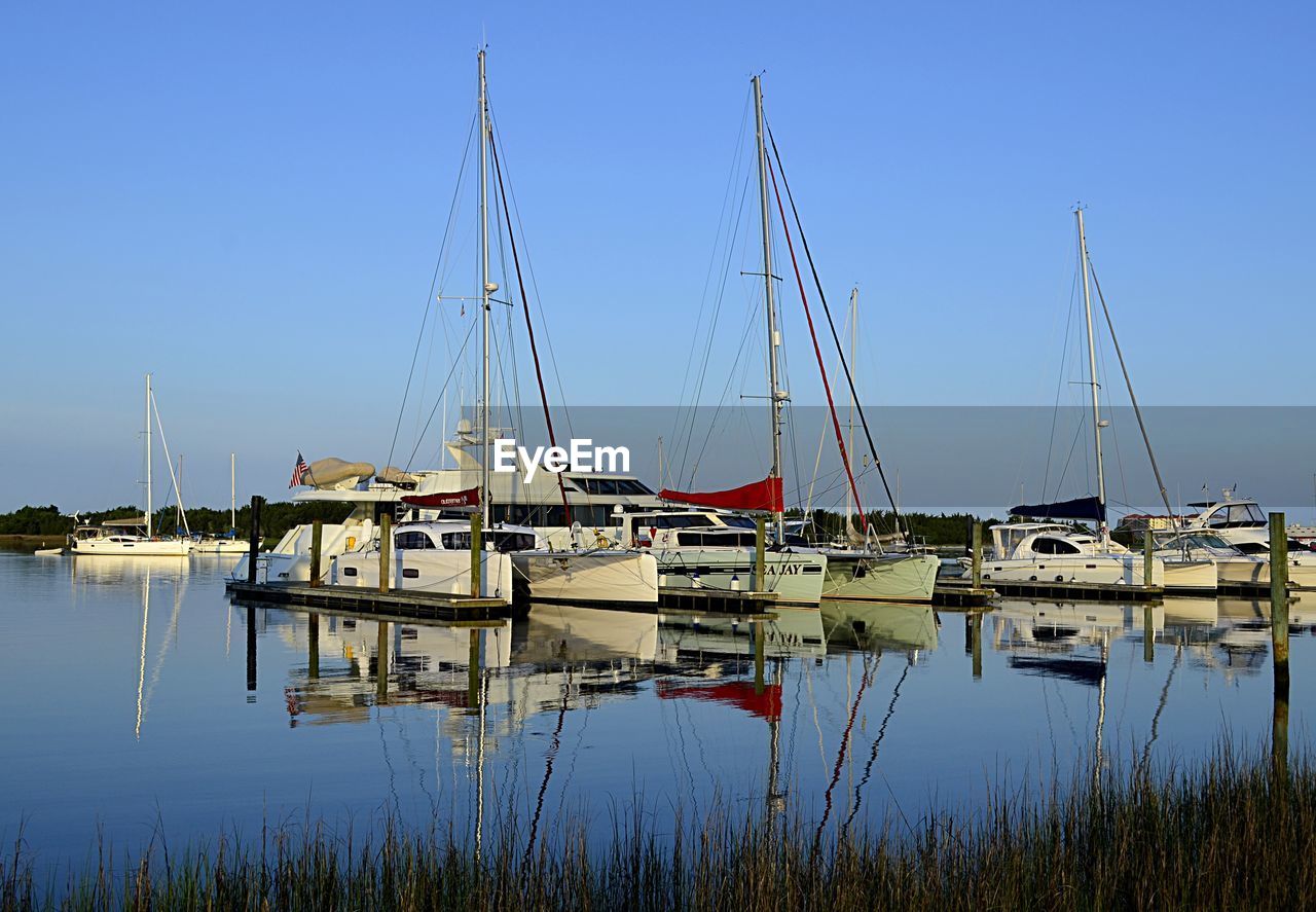 Sailboats moored at harbor against clear blue sky