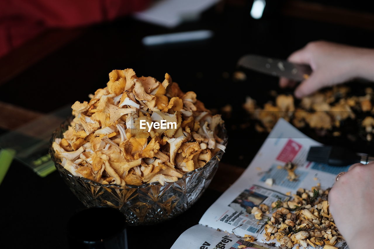 Cropped hands by bowl with edible mushrooms at kitchen