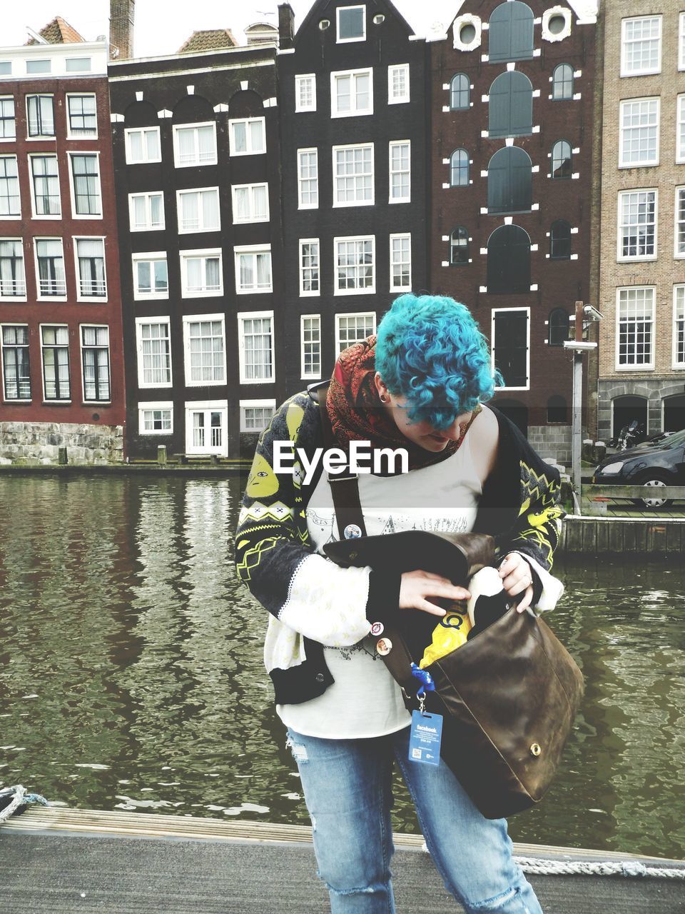 Woman checking her bag while standing near canal against buildings in city