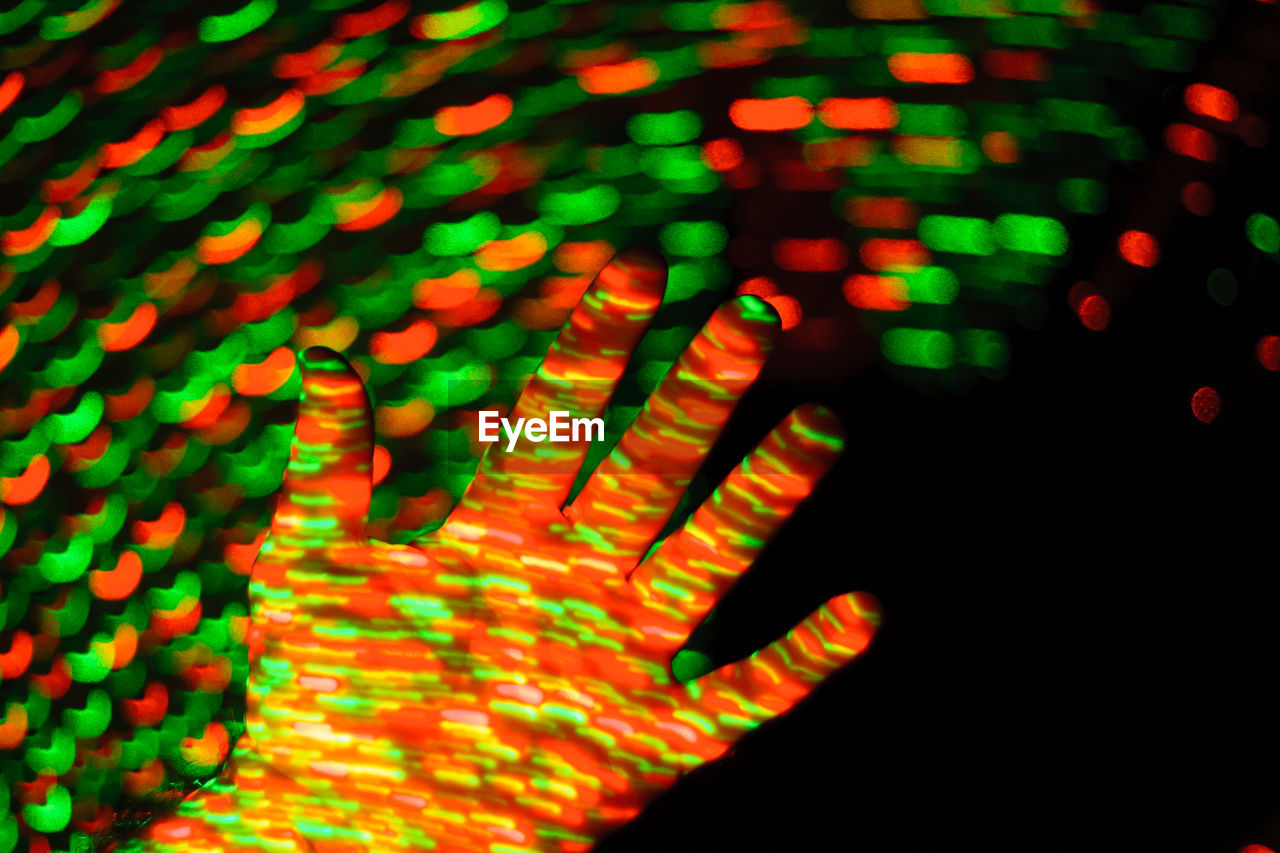 Cropped hand of person with multi colored lights against black background