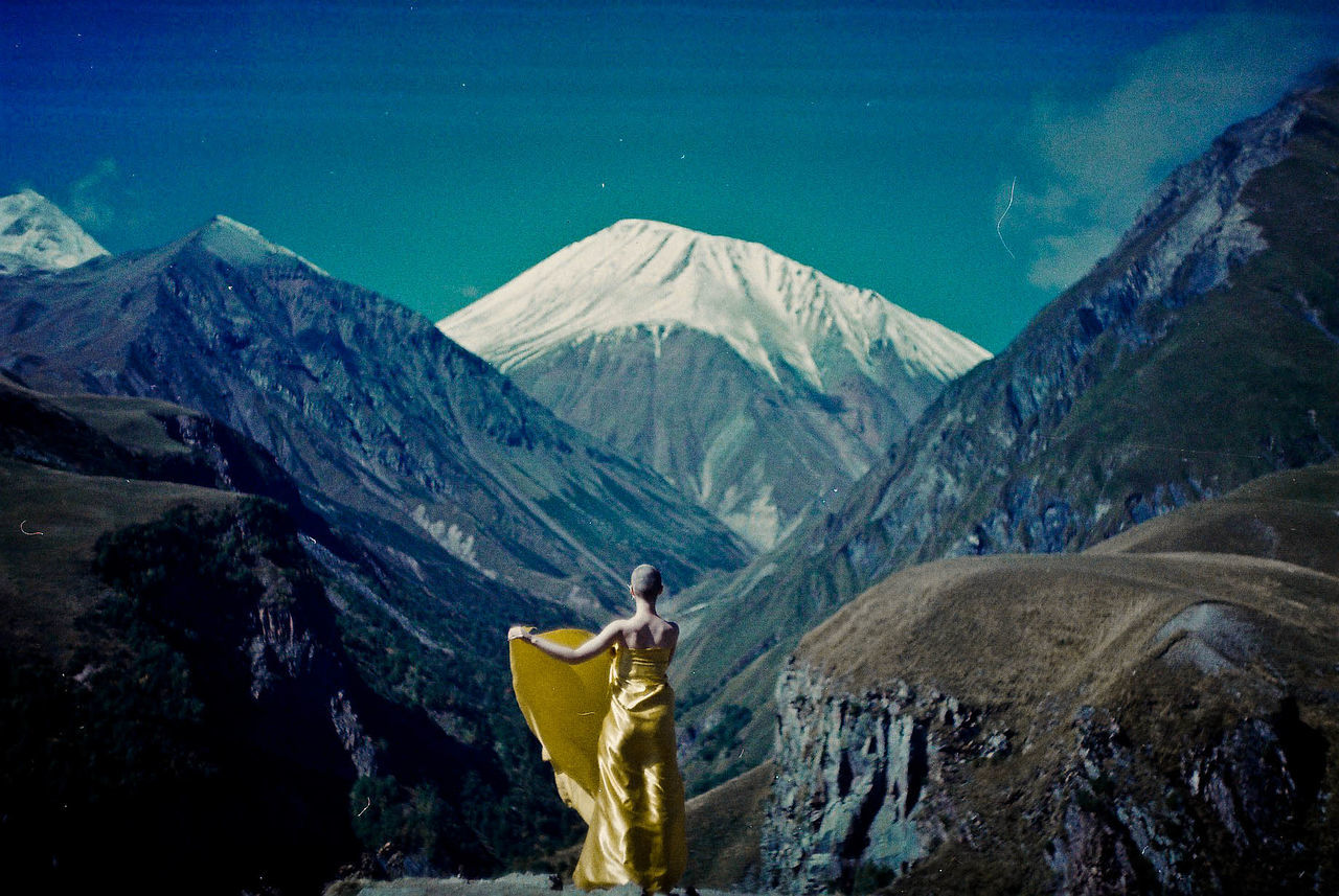 Rear view of bald woman wrapped in yellow textile while standing against mountains