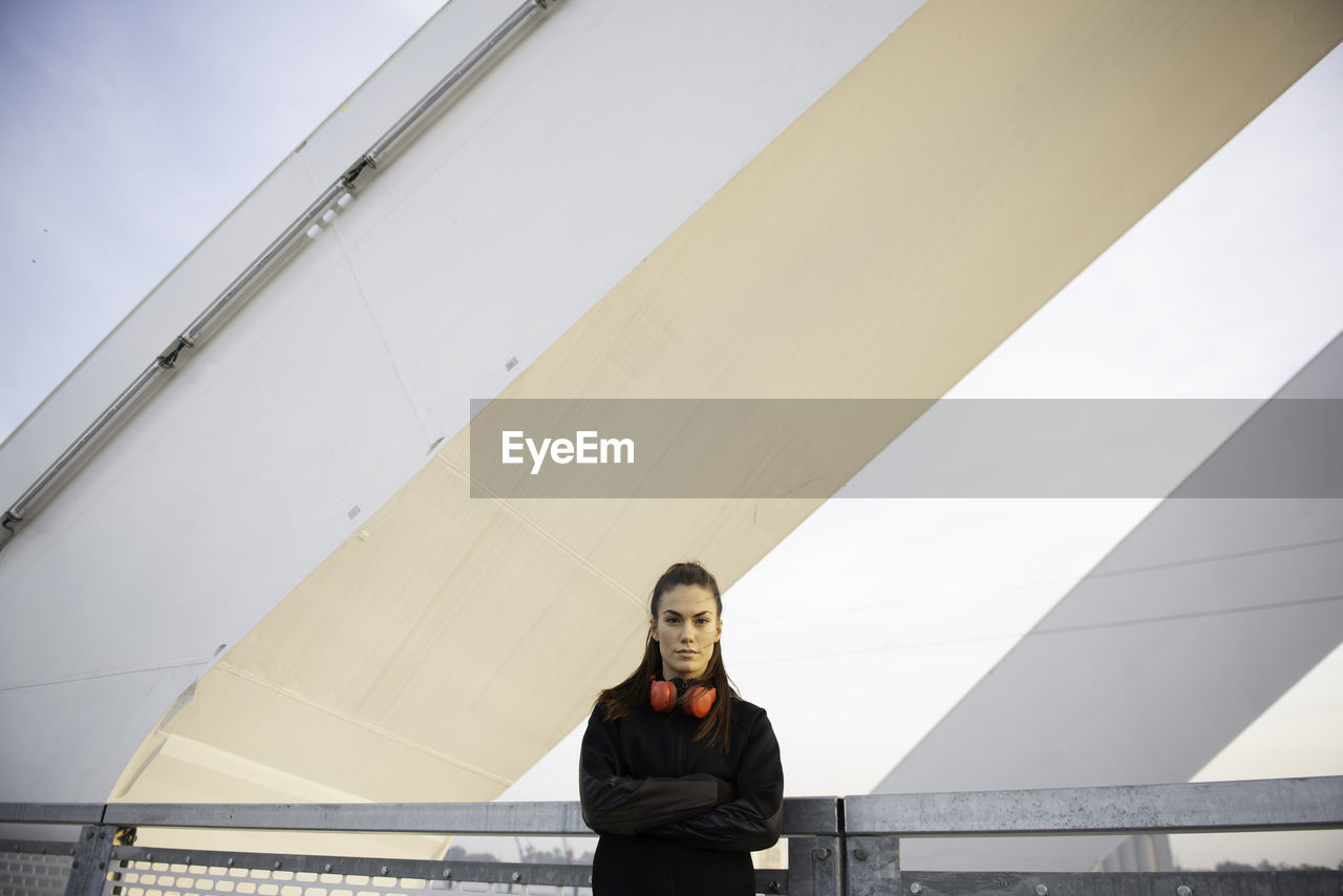 PORTRAIT OF YOUNG WOMAN SITTING ON RAILING AGAINST SKY