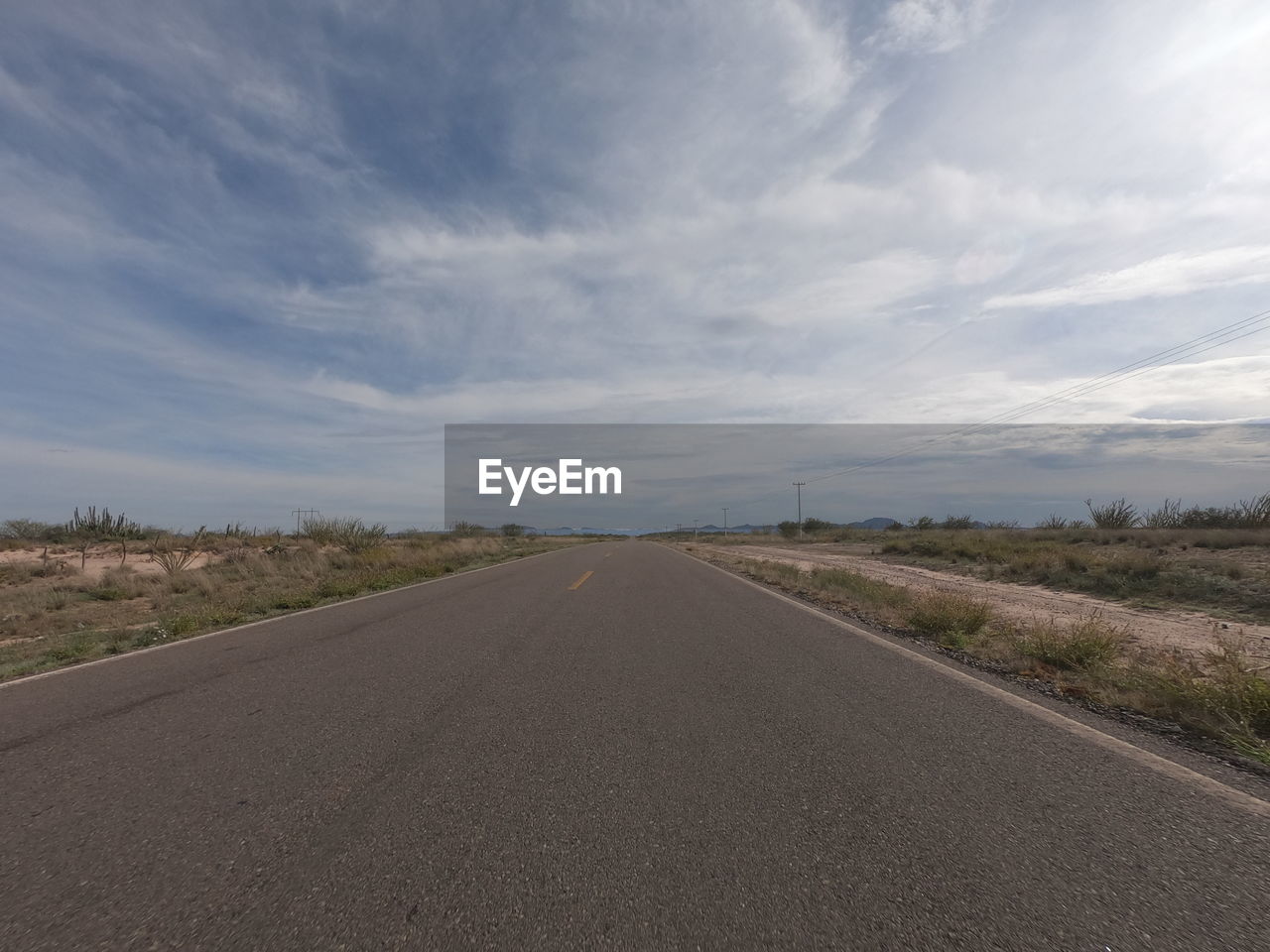 EMPTY ROAD ON FIELD AGAINST SKY