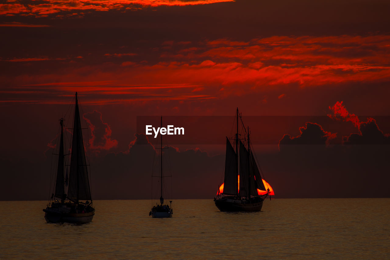 Sailboats sailing on sea against sky during sunset