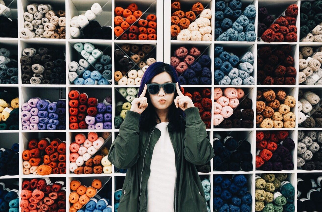 Portrait of young woman standing against colorful wool shelves at store