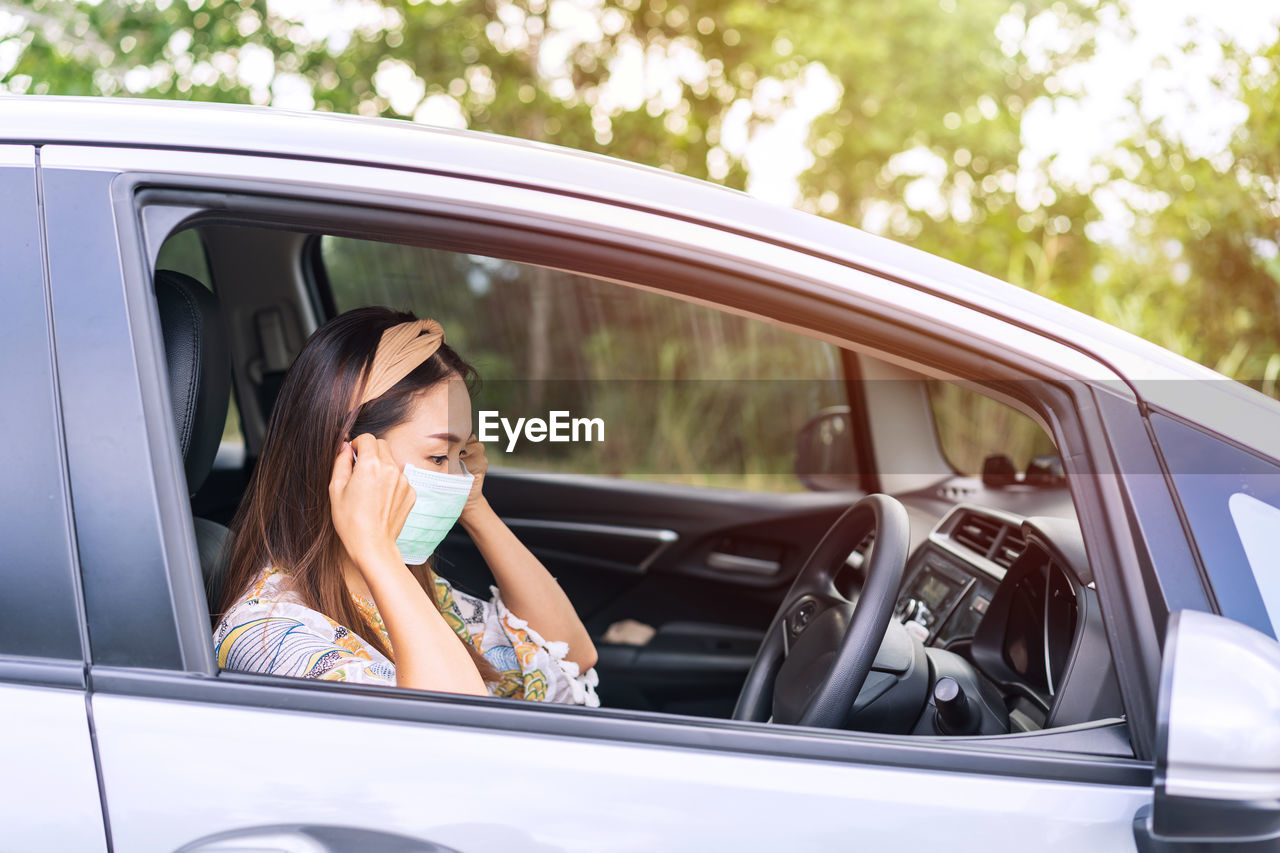 Side view of woman wearing mask sitting in car
