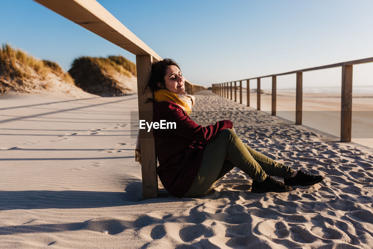 Side view of woman sitting on sand against sky