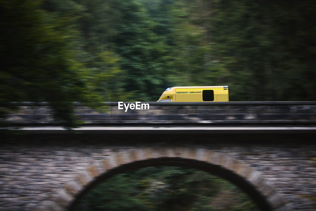 Ambulance car of emergency medical service in blurred motion on stone bridge in mountains. 