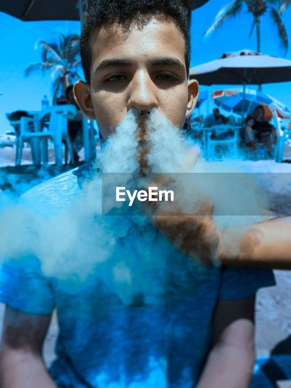 Portrait of young man emitting blue smoke from nose