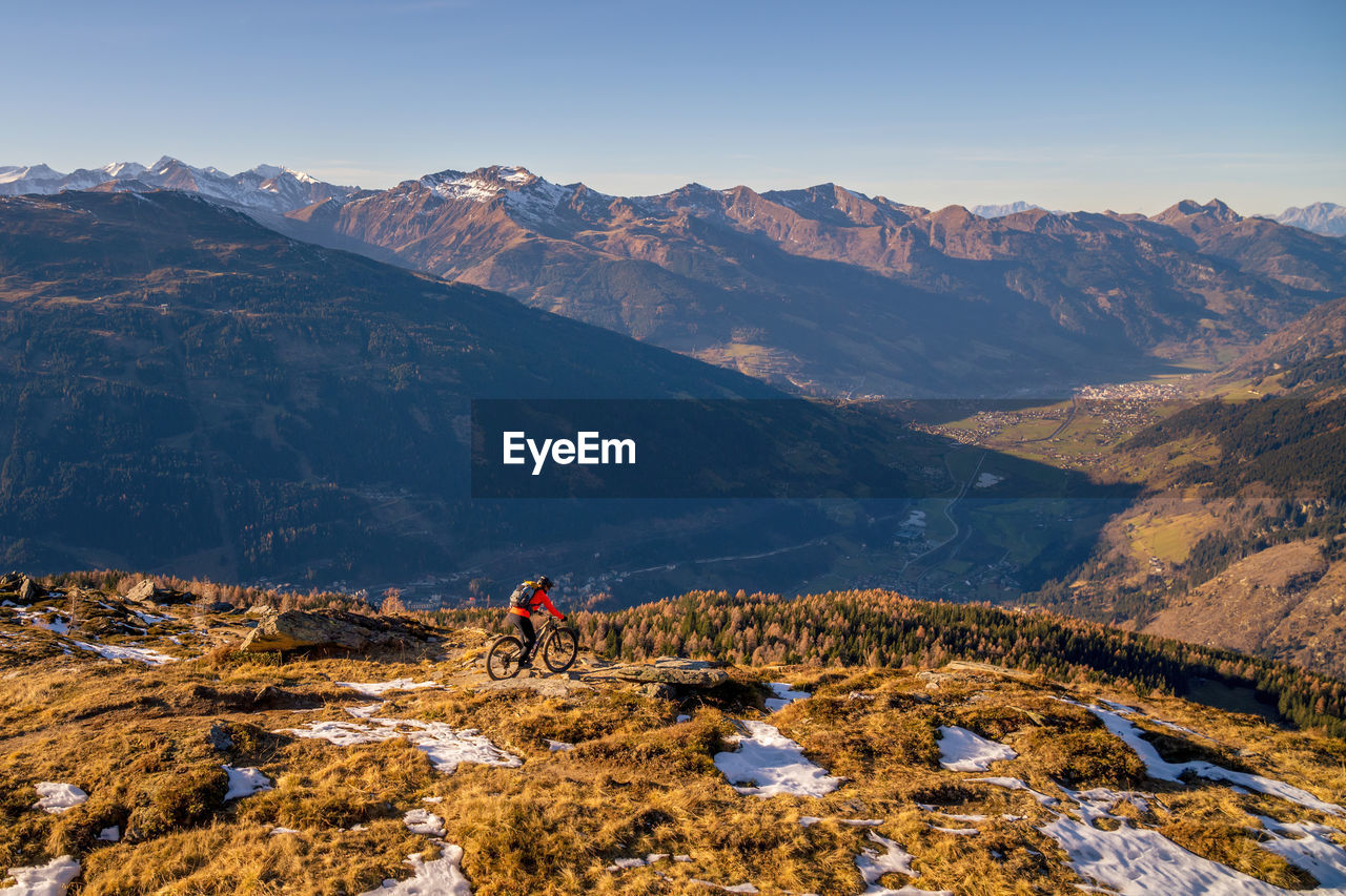 Woman riding a mountain bike on footpath in snow covered alpine terrain, gastein, salzburg, austria.