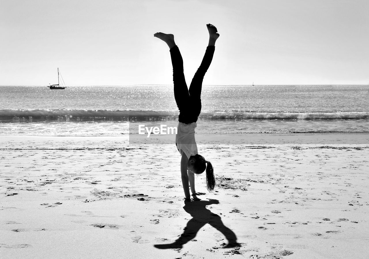 Full length of girl doing handstand at beach against sky