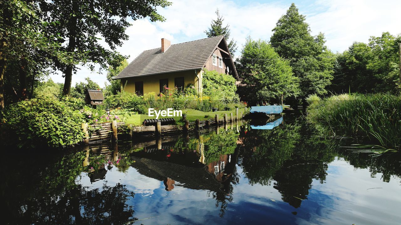 PLANTS BY LAKE AND BUILDING AGAINST SKY