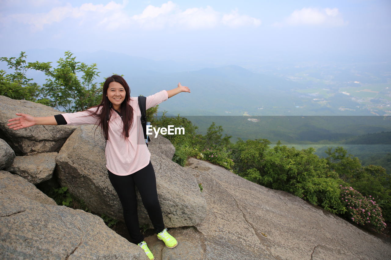 Portrait of woman with arms outstretched standing on mountain against sky