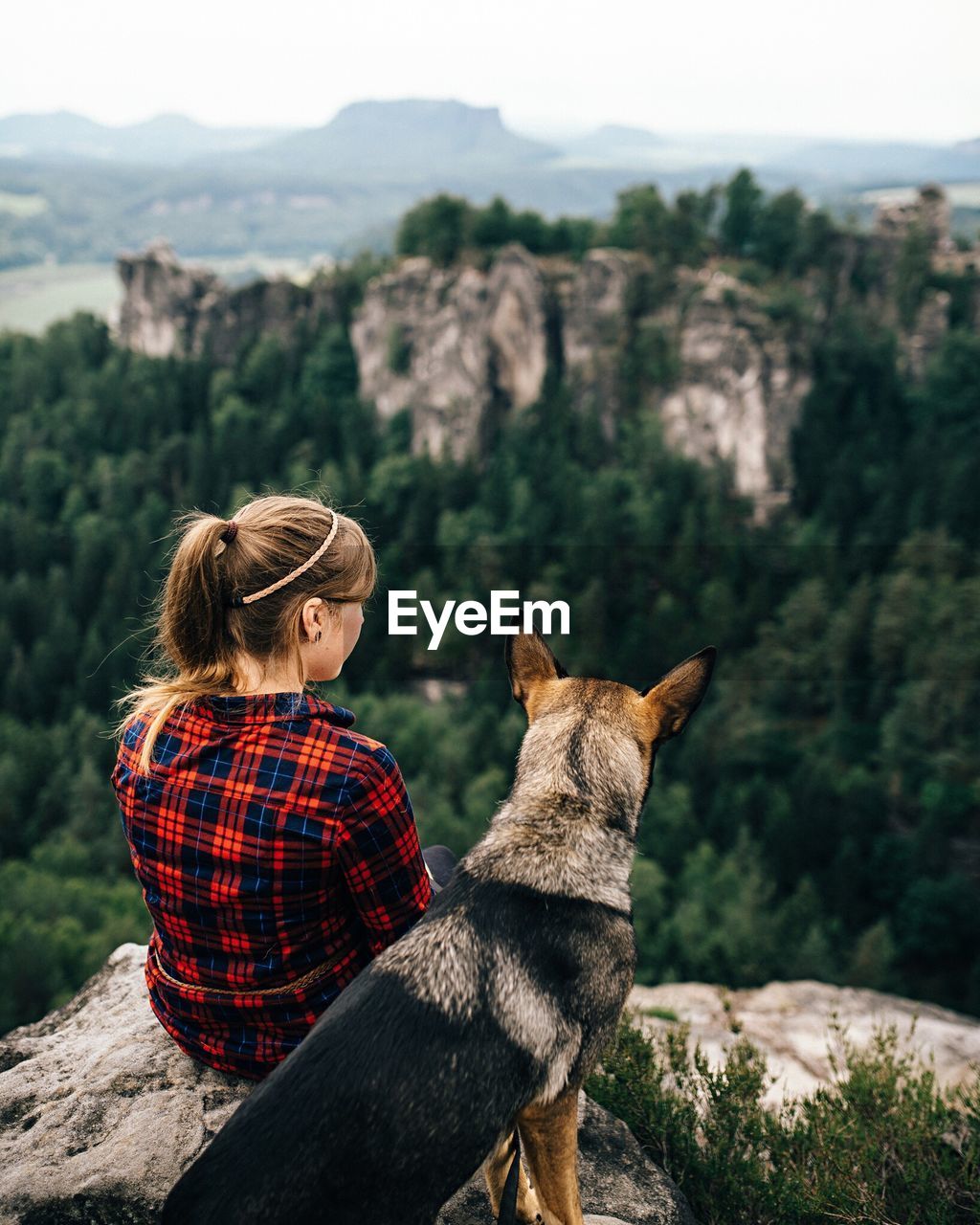 Rear view of woman sitting with dog at mountain peak