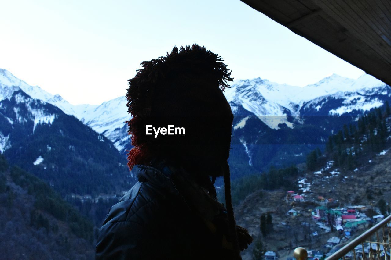 REAR VIEW OF MAN LOOKING AT SNOWCAPPED MOUNTAIN