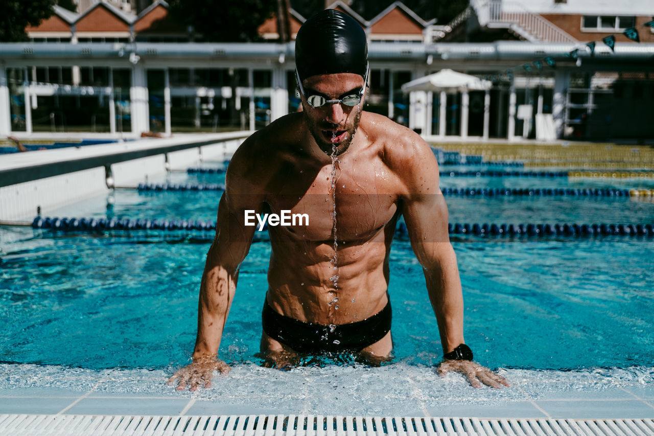 Muscular male swimmer getting out from swimming pool on sunny day