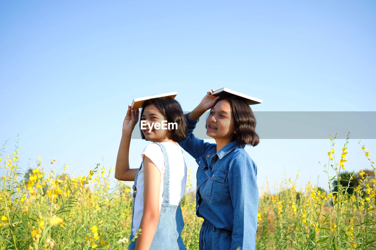 Smiling teenage girls carrying book on head