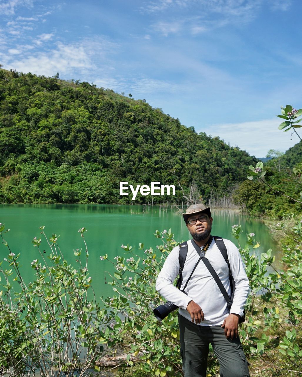 Portrait of young man standing at lakeshore against mountain