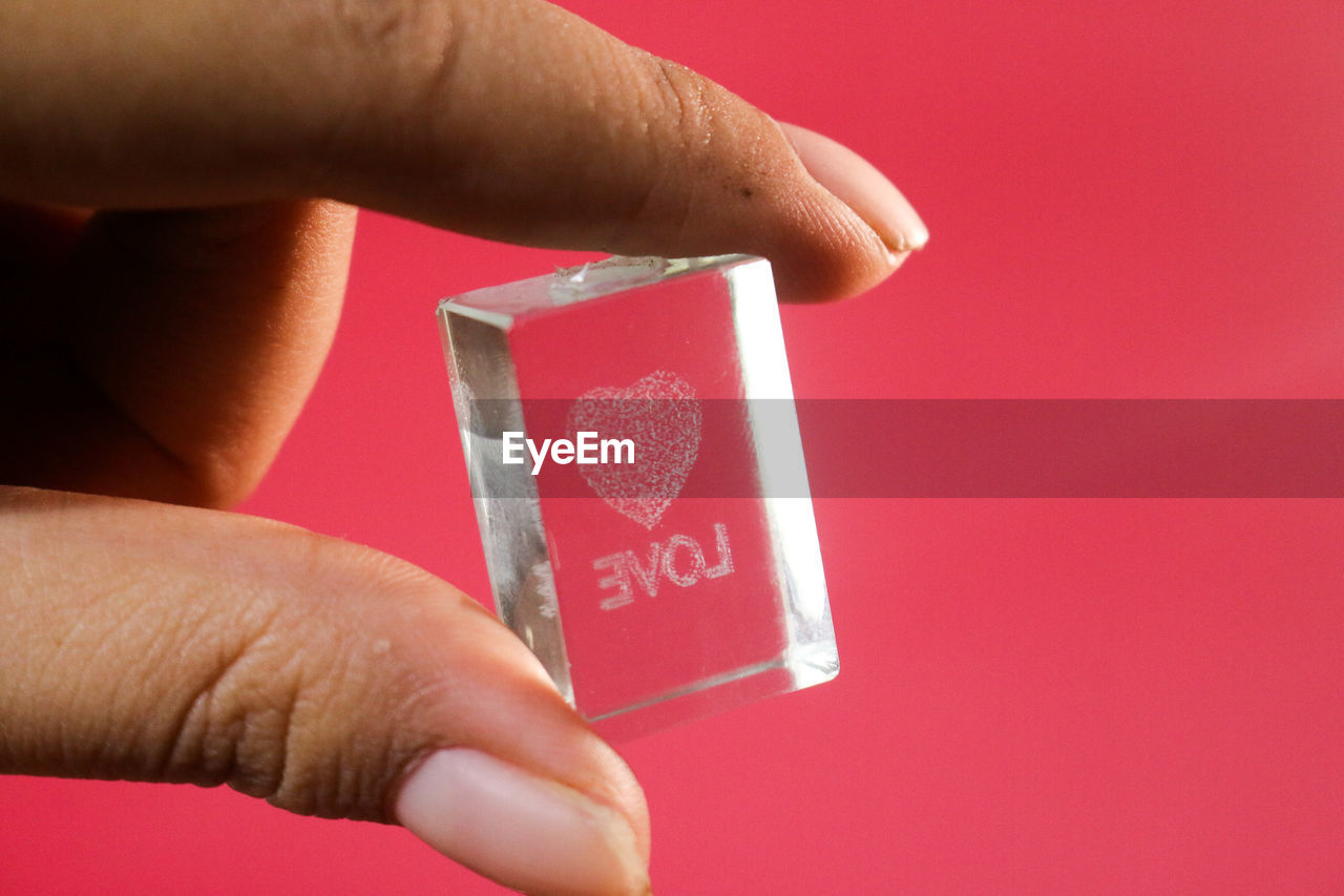 CLOSE-UP OF HAND HOLDING RED PAPER OVER WHITE BACKGROUND