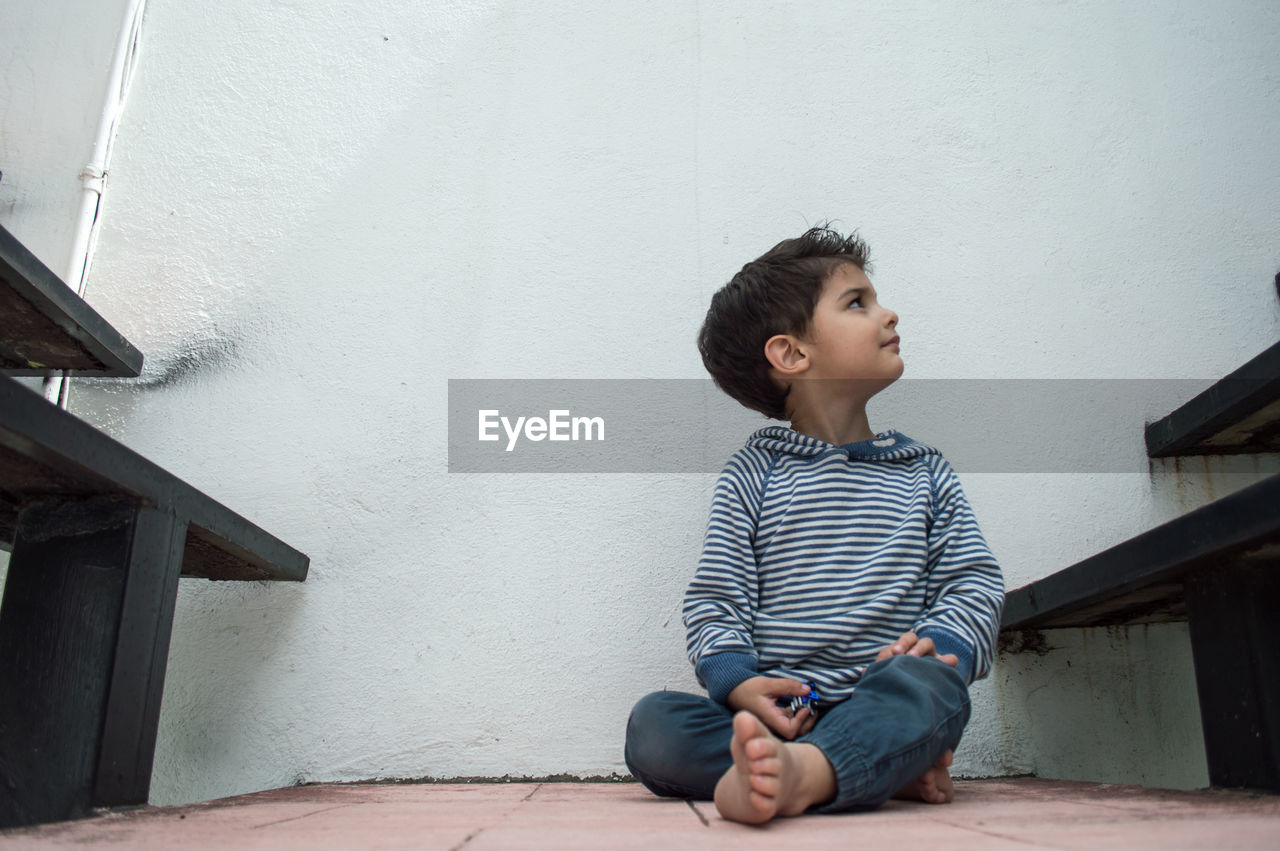 BOY LOOKING AWAY SITTING ON WALL