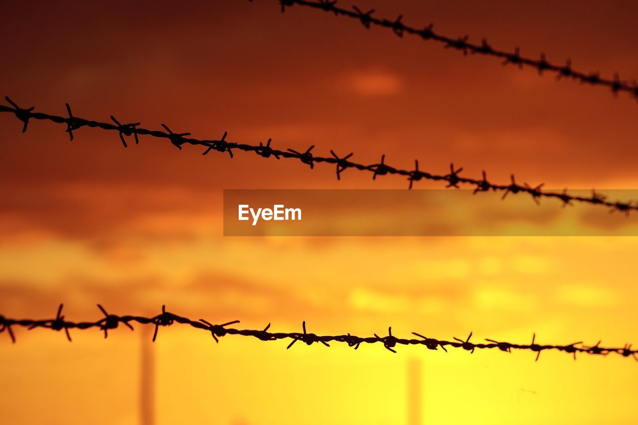 BARBED WIRE FENCE AGAINST SKY DURING SUNSET