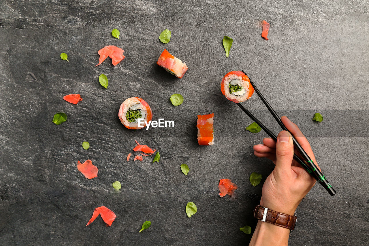 Cropped image of man holding sushi with chopsticks on stone tray