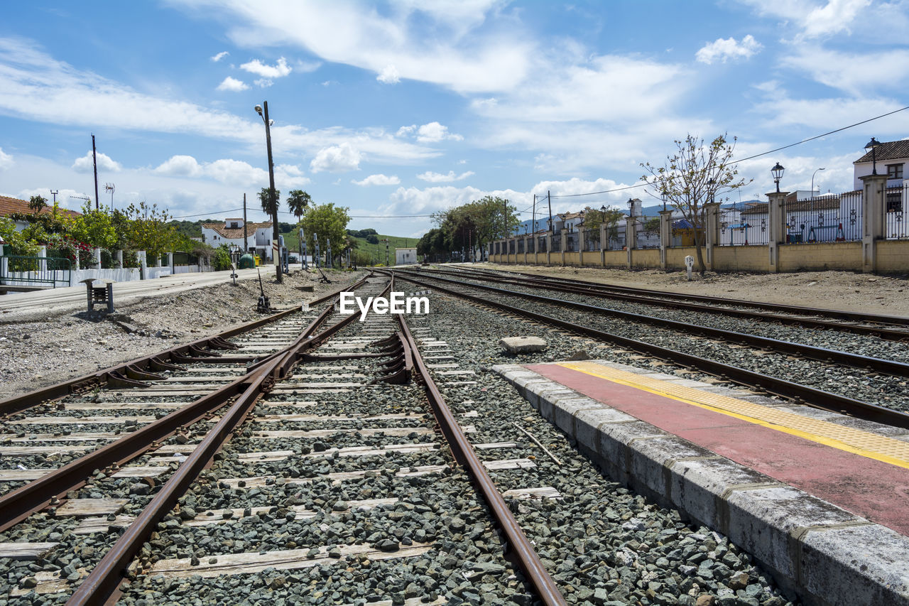 railroad track, track, rail transportation, sky, transportation, railway, transport, cloud, mode of transportation, architecture, vehicle, train station, nature, public transportation, railroad station, train, travel, day, no people, city, residential area, built structure, outdoors, railroad station platform, metropolitan area, building exterior, tree, sunlight, vanishing point, travel destinations