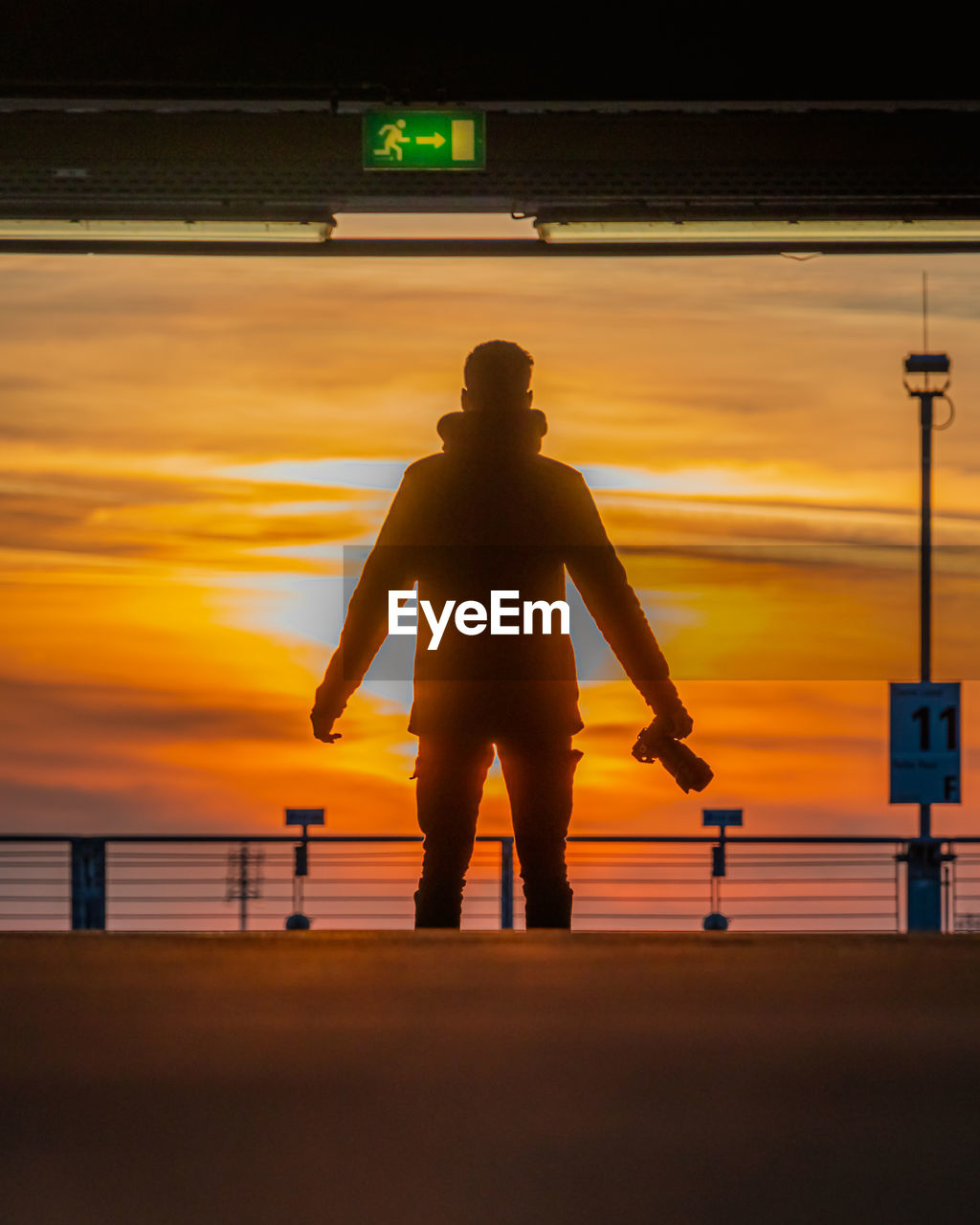 sunset, silhouette, sky, one person, evening, light, yellow, standing, nature, transportation, men, orange color, adult, reflection, person, rear view, dusk, architecture, cloud, sun, full length, lifestyles, outdoors, sign, water, backlighting, city, travel