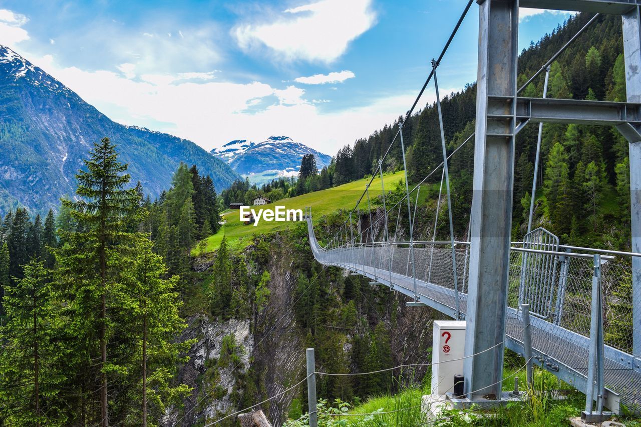 Footbridge by trees against mountain