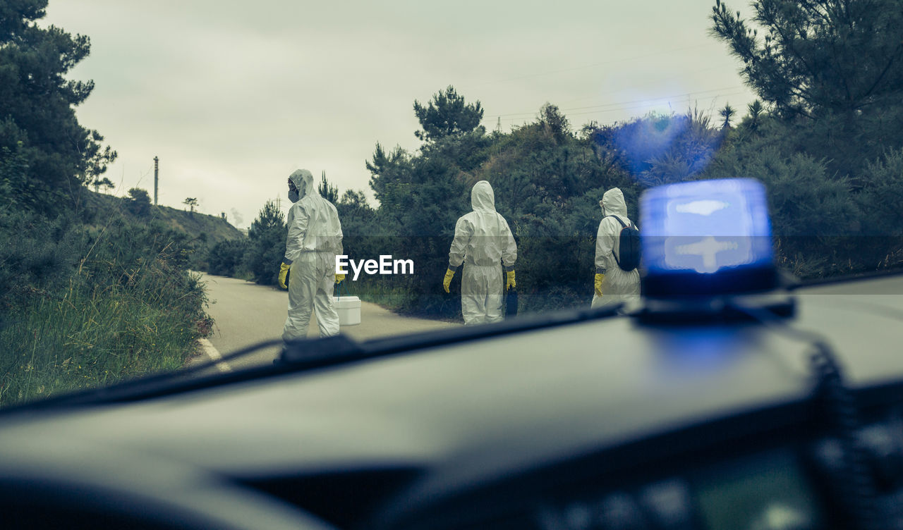 Rear view of people wearing protective suit walking on road seen through car