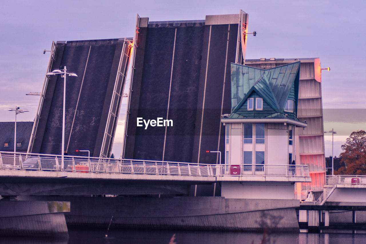 BRIDGE OVER RIVER BY BUILDING AGAINST SKY