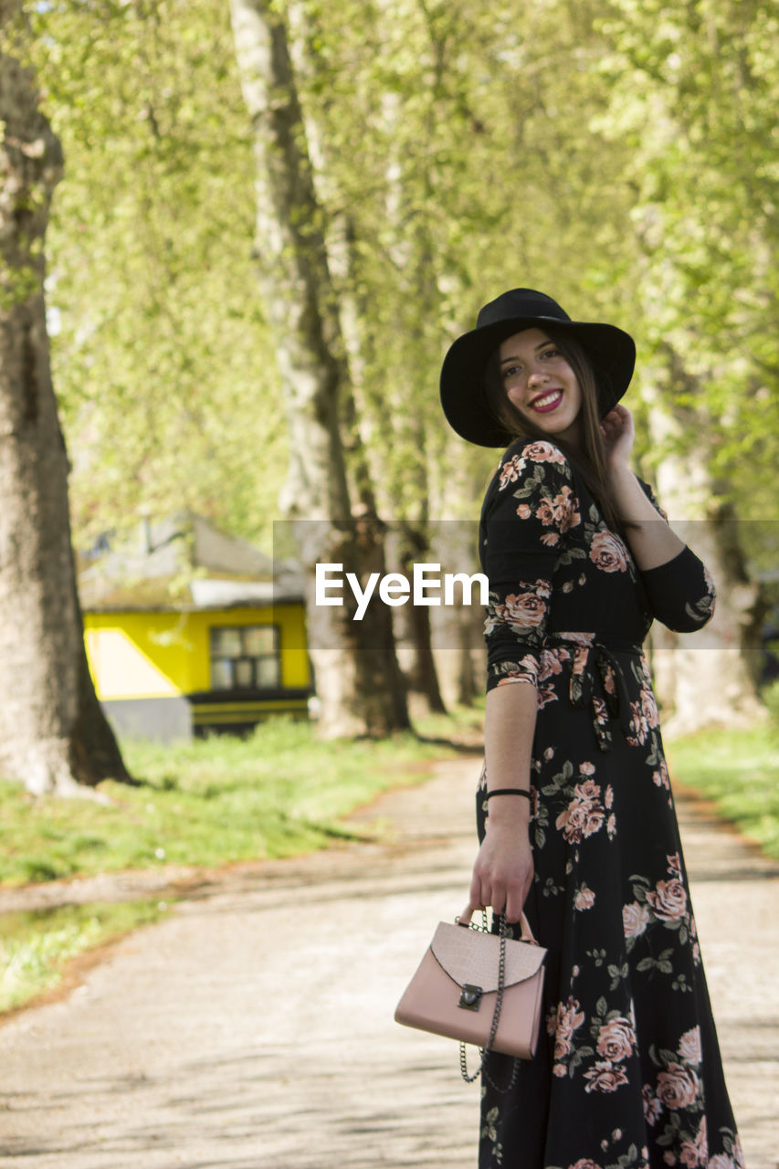 Portrait of smiling woman wearing hat standing against trees