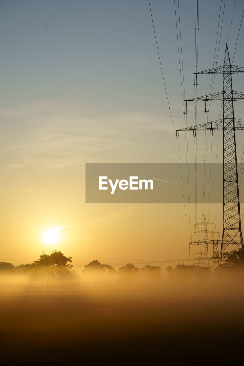 ELECTRICITY PYLONS ON LANDSCAPE AGAINST SKY AT SUNSET