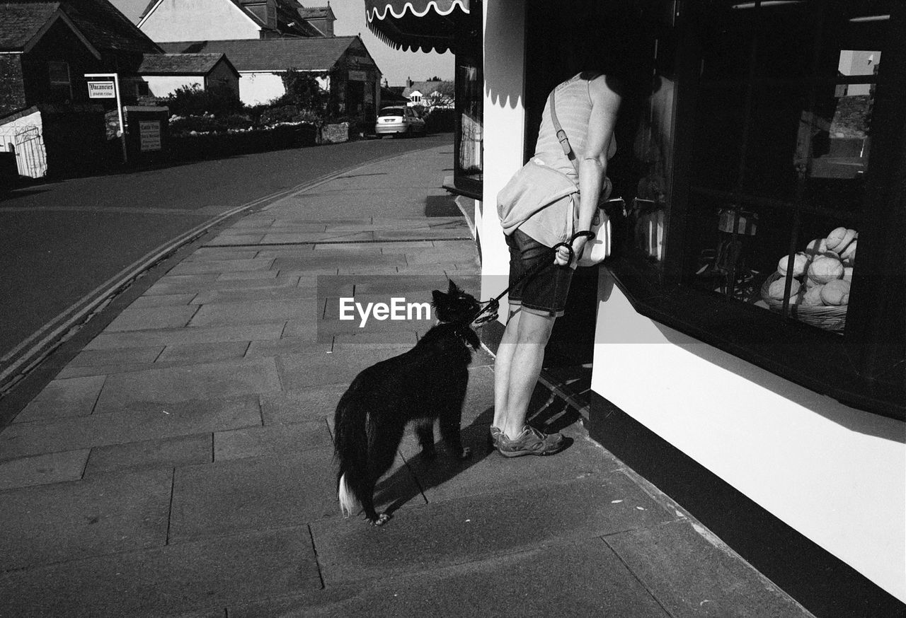 Full length of woman with dog standing near door at sidewalk