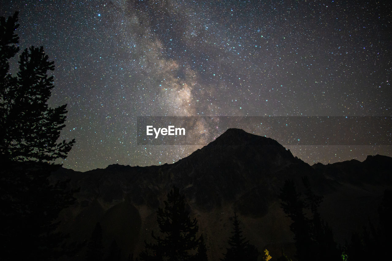 LOW ANGLE VIEW OF SILHOUETTE MOUNTAIN AGAINST STAR FIELD