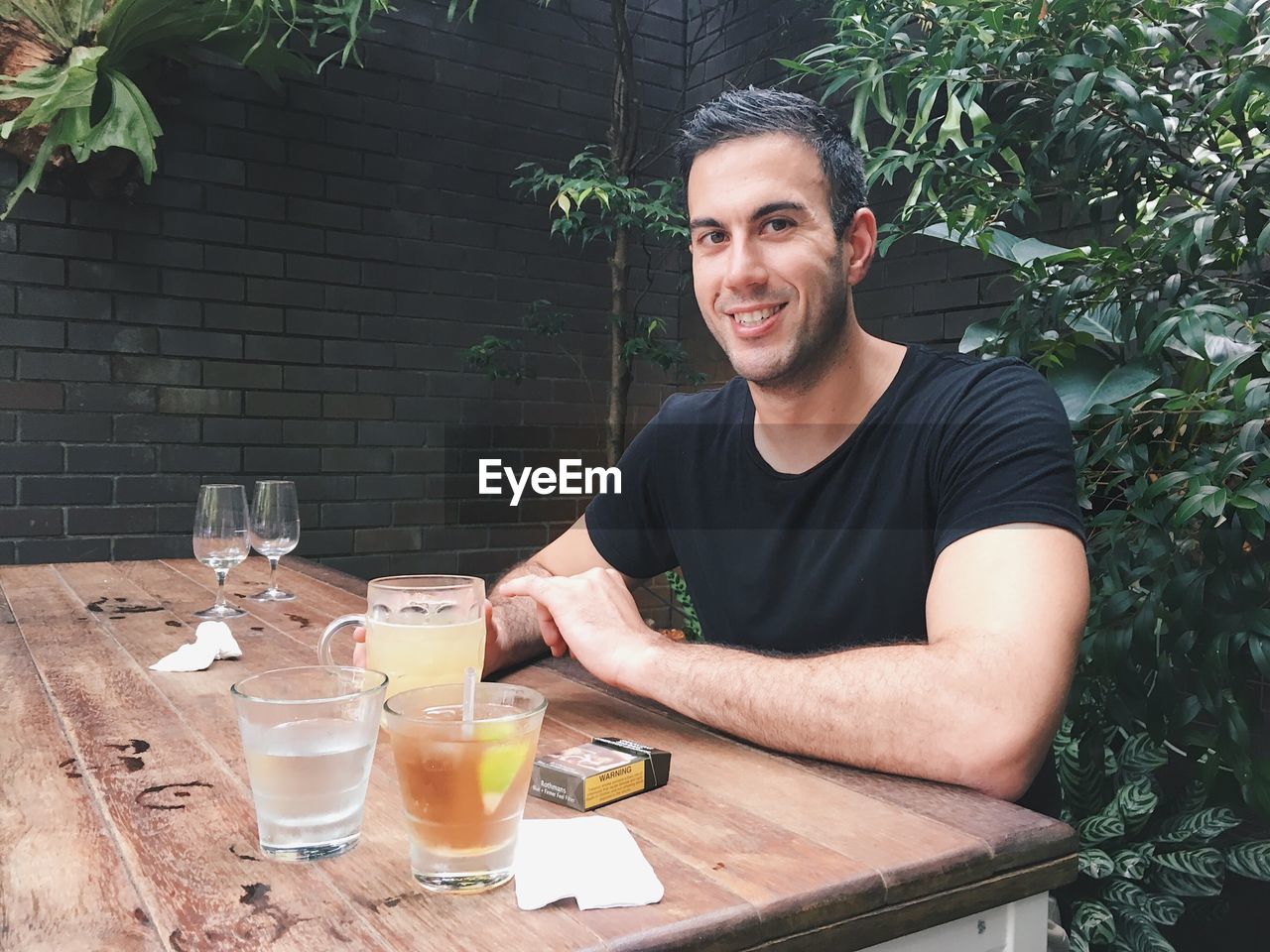 PORTRAIT OF SMILING YOUNG MAN SITTING ON TABLE