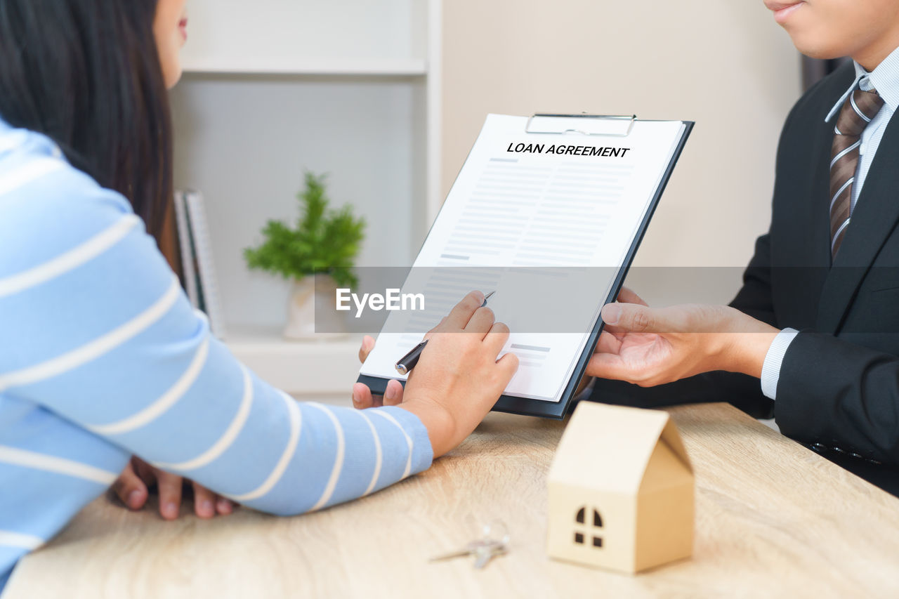 Midsection of woman signing agreement paper held by businessman in office