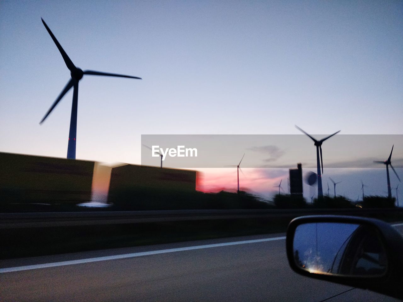Wind turbines by street against sky during sunset