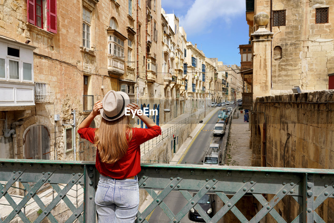 Tourist woman holds hat on iron bridge looking the old town of valletta, malta