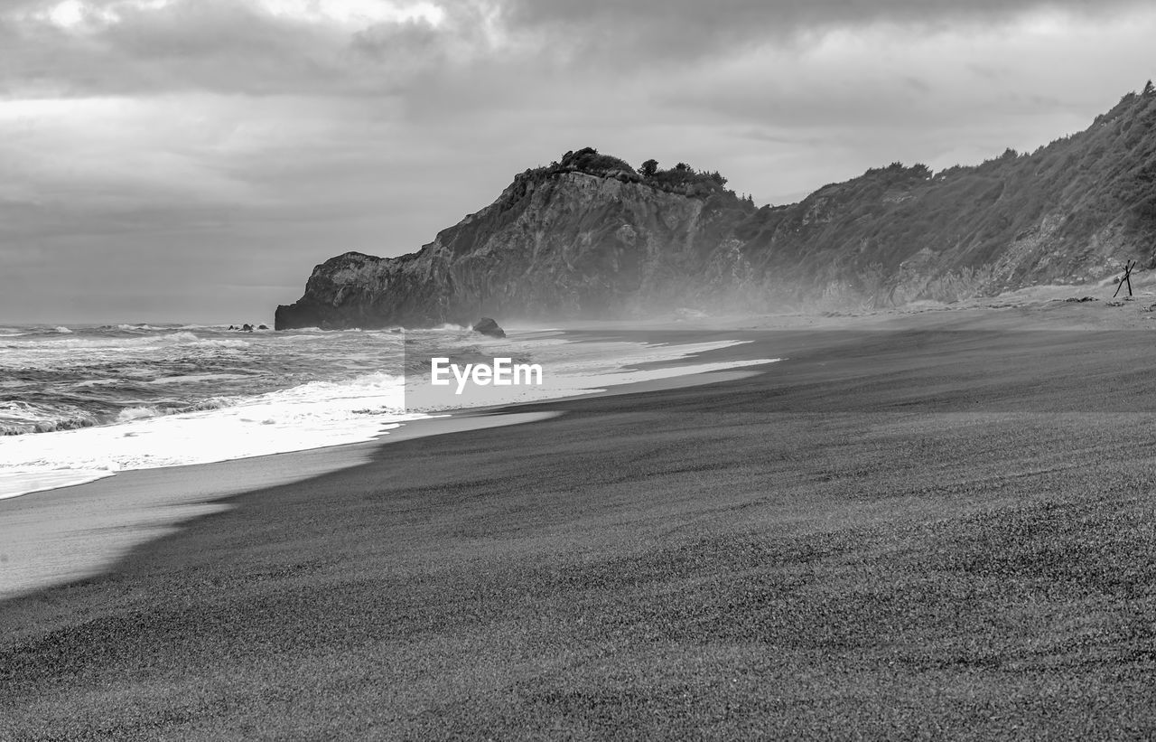 land, beach, sea, water, coast, wave, sky, ocean, scenics - nature, sand, shore, beauty in nature, black and white, cloud, nature, environment, body of water, horizon, wind wave, landscape, monochrome, monochrome photography, rock, coastline, travel destinations, motion, travel, mountain, tranquility, bay, sports, no people, terrain, outdoors, holiday, tranquil scene, cliff, seascape, water sports, trip, tourism, vacation, water's edge, non-urban scene, day